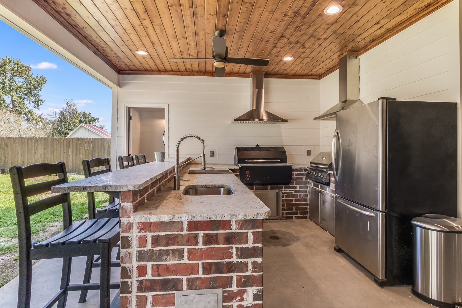 outdoor kitchen with fridge, two grills, sink, and chairs