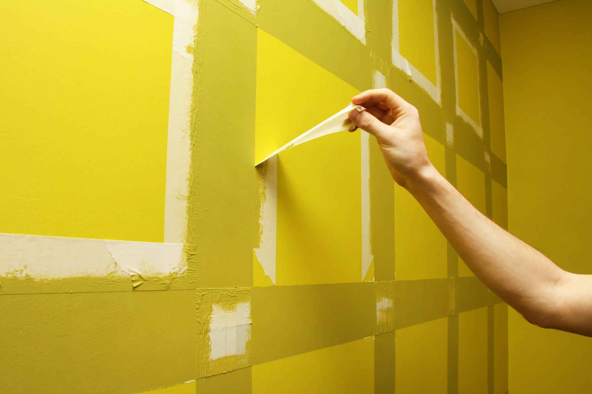 worker,man,removing,masking,tape,from,painting,wall