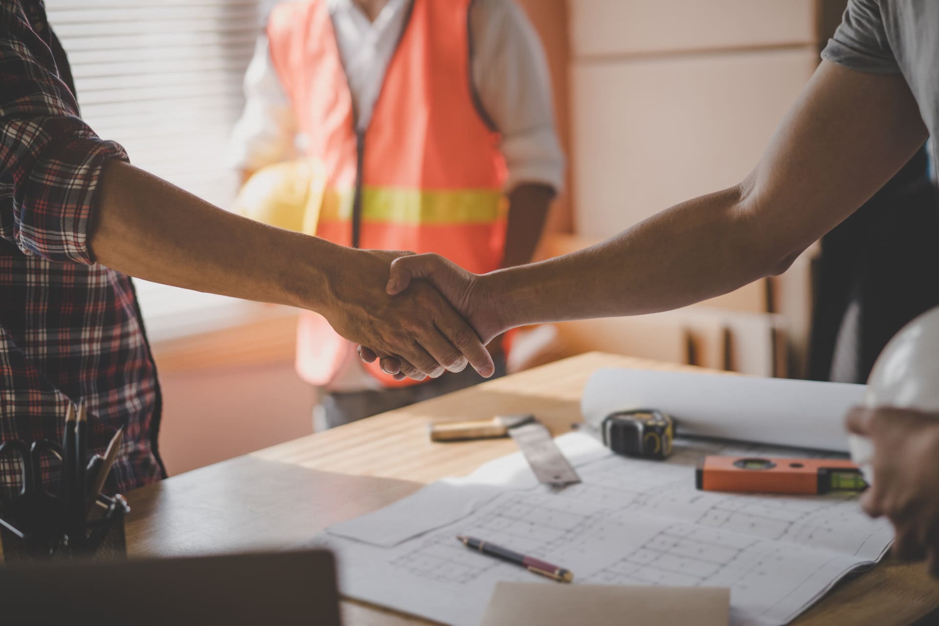 two construction workers shaking hands in front of a desk.