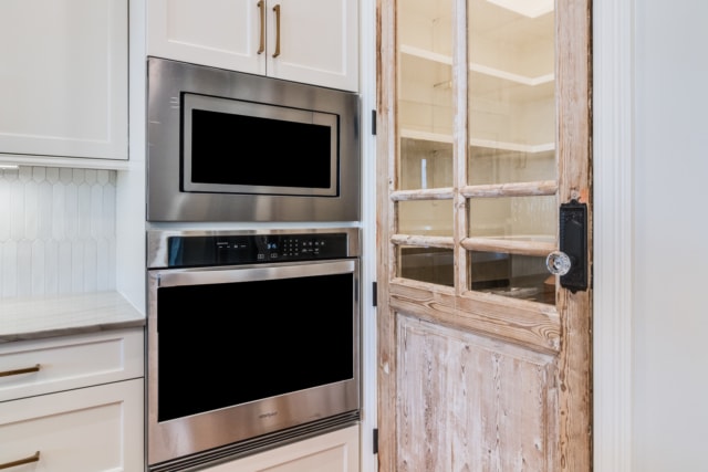 a white kitchen with a wooden door and a microwave.