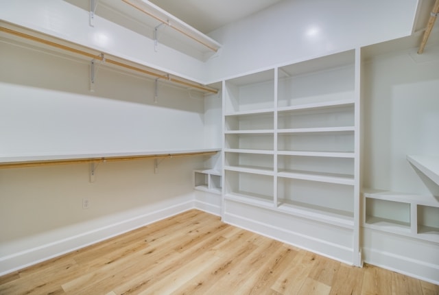 a walk in closet with white shelves and wood floors.