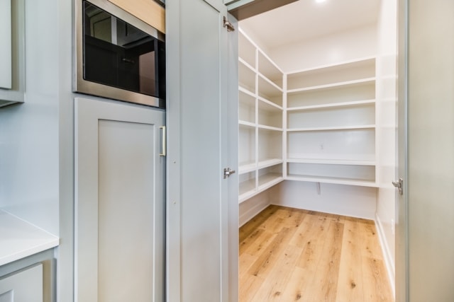 a walk in pantry with white cabinets and wood floors.