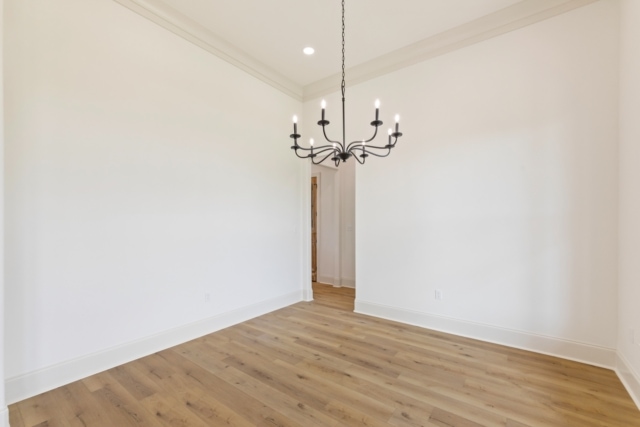 an empty room with hardwood floors and a chandelier.