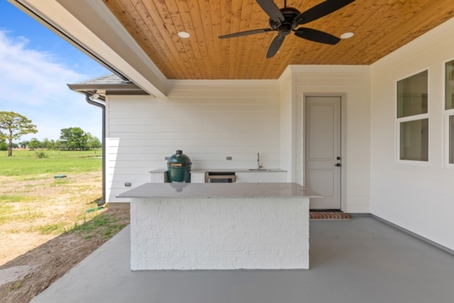an outdoor kitchen with a ceiling fan and a grill.