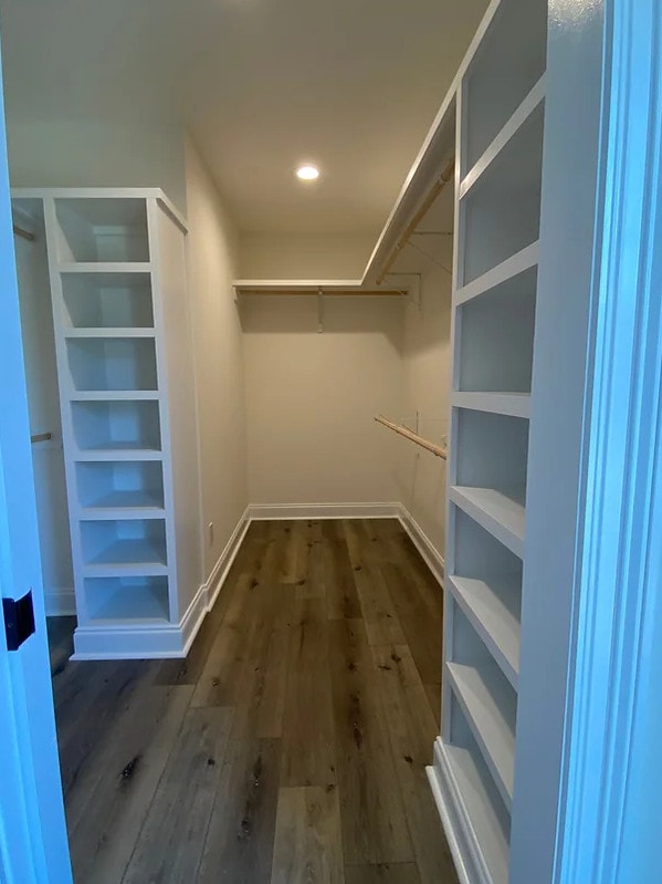 a walk in closet with shelves and a wooden floor.