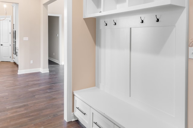 a white mudroom with white cabinets and a wooden floor.