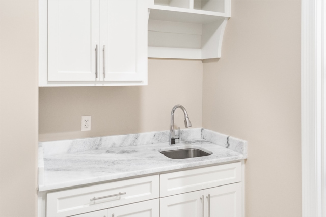 a laundry room with white cabinets and marble counter tops.