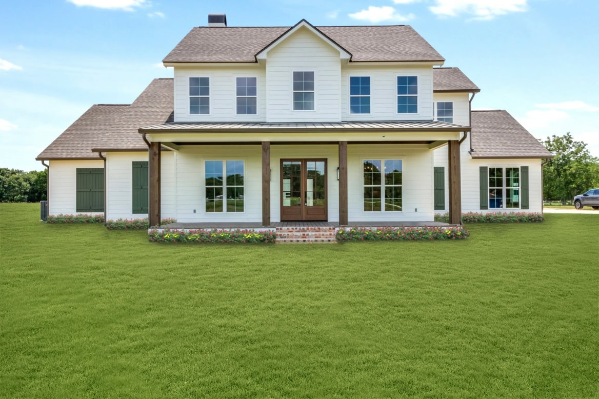 A two-story, white Waltman house with a grey roof, a front porch with wooden pillars, and multiple windows. The house is set on a well-maintained lawn with flowers along the front edge. A vehicle is partially visible on the right. The sky is clear and sunny.