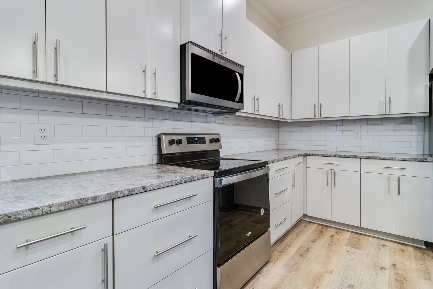 Modern kitchen with white cabinets, stainless steel appliances, a subway tile backsplash, gray marbled countertops, and light wood flooring. The area appears clean and uncluttered.