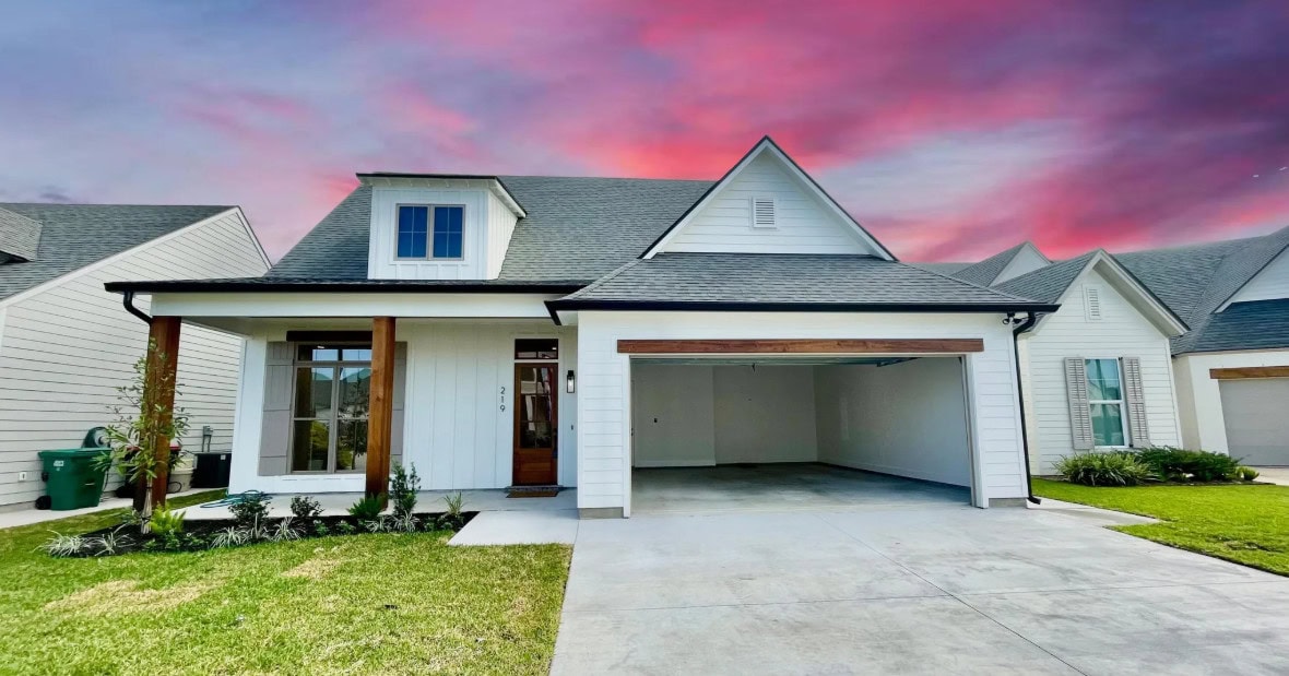 A modern white house with a two-car garage, gabled roof, covered entryway, and manicured front lawn. The sky is pink and purple, indicating either sunrise or sunset.