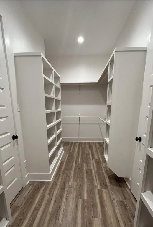 A spacious walk-in closet with built-in white shelves on both sides, wood-patterned flooring, a hanging rod, and white walls under bright ceiling lighting.