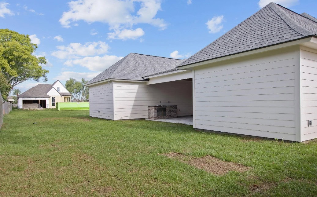 Two white detached garage structures with gray roofs stand on a grassy backyard. One garage has an open bay revealing a built-in grill. A neighboring house and trees are visible in the background under a blue sky.