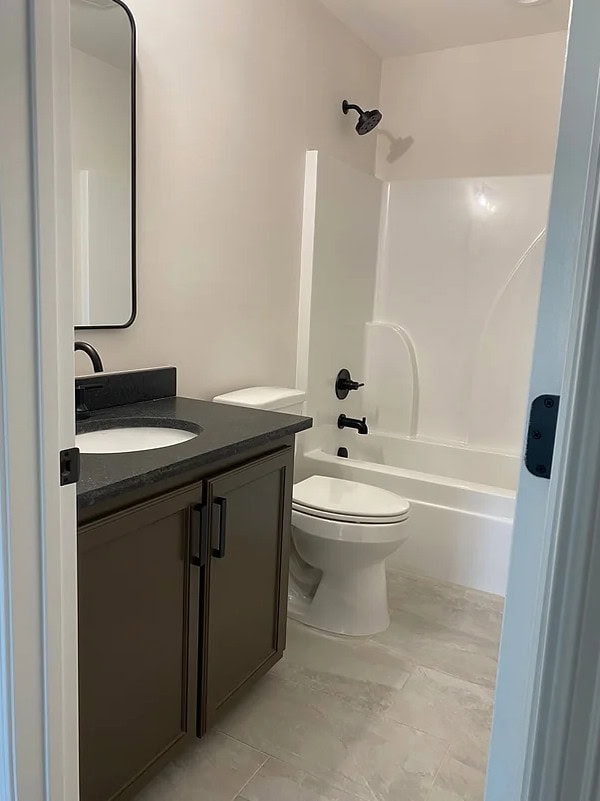 A small bathroom with light-colored tile flooring, a dark vanity with a sink and black faucet, a white toilet, and a white bathtub-shower combo with black fixtures. A rectangular mirror hangs above the sink.