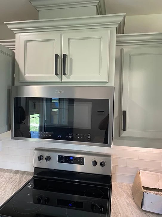 A microwave oven is installed directly above a stove, with cabinet doors above it that cannot open fully due to the microwave's placement. There is a cardboard box on the right side of the marble countertop.