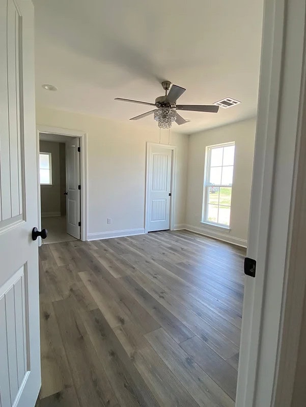 A bright, empty room with light-colored wood flooring, off-white walls, a ceiling fan with light, two closets with white doors, and a large window letting in natural light.