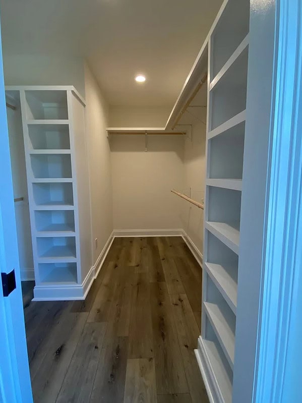A walk-in closet with built-in white shelves and hanging rods on both sides, hardwood flooring, and white walls, illuminated by a ceiling light.
