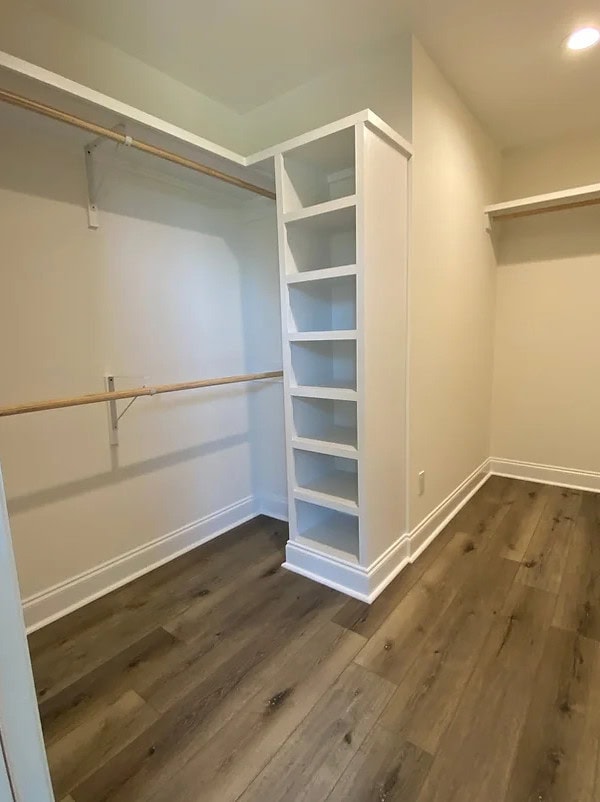 A walk-in closet with light-colored walls, wood flooring, open shelves in the center, and wooden hanging rods on both sides. The space is empty and well-lit.