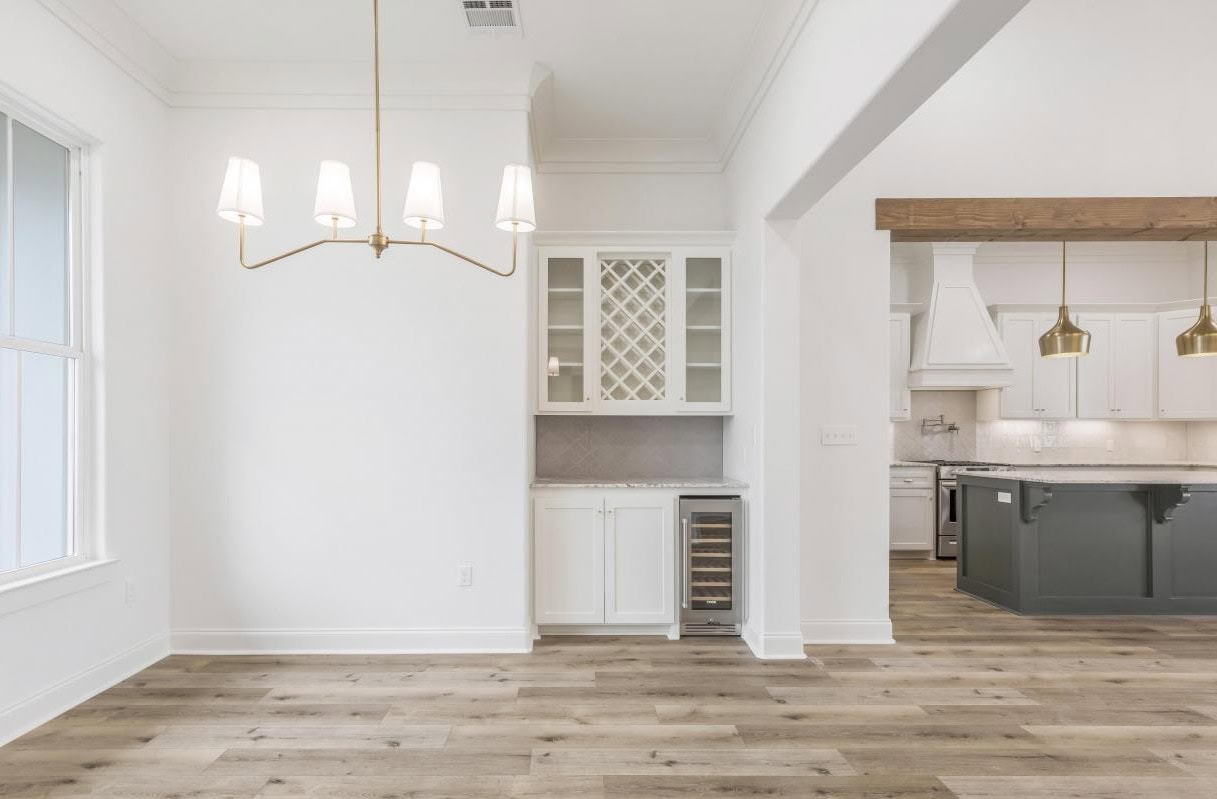 Bright, modern kitchen and dining area with wood flooring, a gold chandelier, built-in wine rack and beverage fridge, white cabinets, and an adjacent kitchen island with pendant lights.