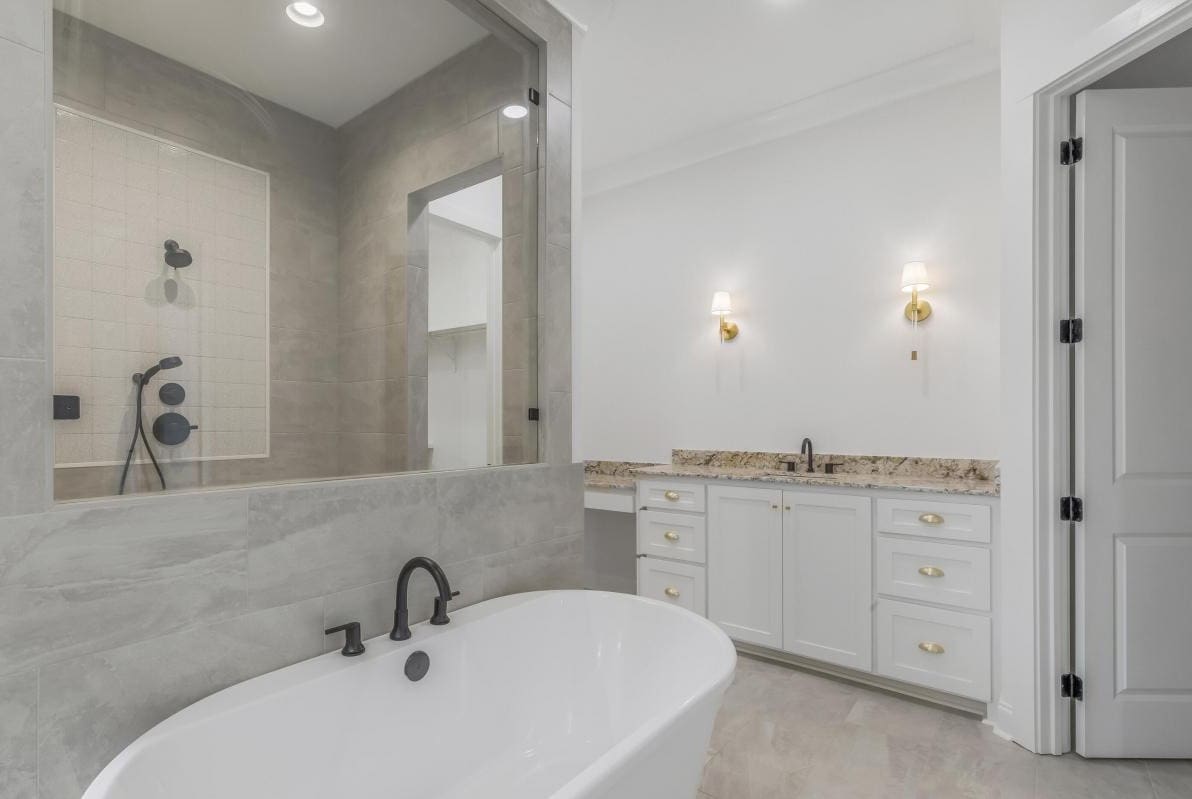 Modern bathroom with a white freestanding tub, black fixtures, a glass-enclosed shower, dual sinks with marble counters, white cabinets with gold handles, and two wall-mounted lights above the vanity.