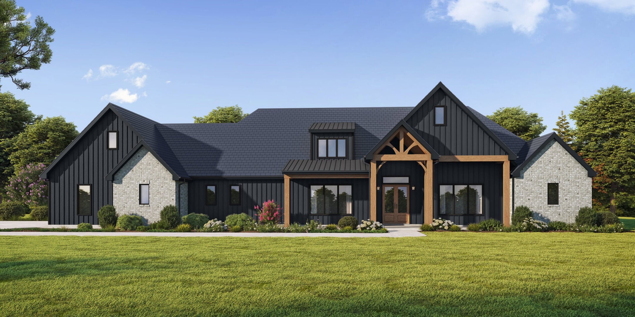 A modern farmhouse with dark siding, stone accents, a gabled roof, and a covered entry supported by wood beams. The house is surrounded by green lawn, shrubs, and trees under a blue sky with scattered clouds.