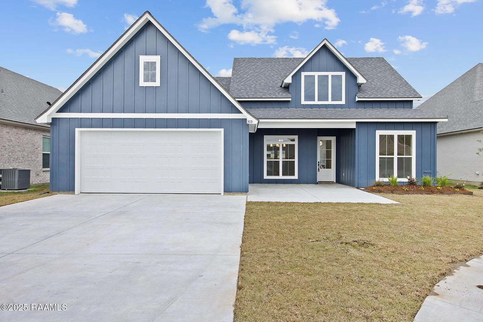 A two-story blue house with white trim, a double garage, front porch, and a small lawn, set against a partly cloudy sky.