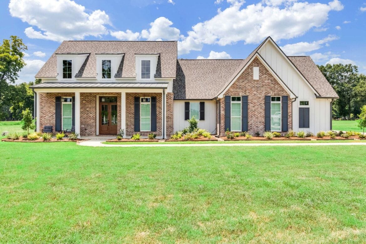 A large, single-story brick and white siding home with a front porch, dormer windows, and a green lawn.