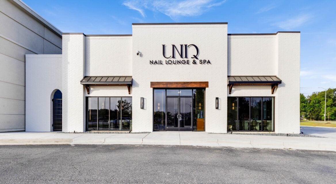 The exterior of UNIQ Nail Lounge & Spa, featuring a white brick building with large glass windows and a centered double door entrance.