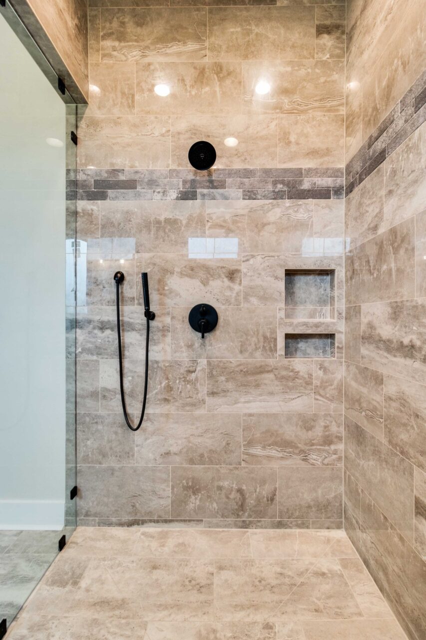 Walk-in shower with beige stone-look tile, a built-in recessed shelf, and matte black plumbing fixtures.