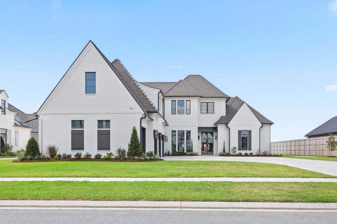A two-story white brick house with a multi-gabled roof and a front lawn.