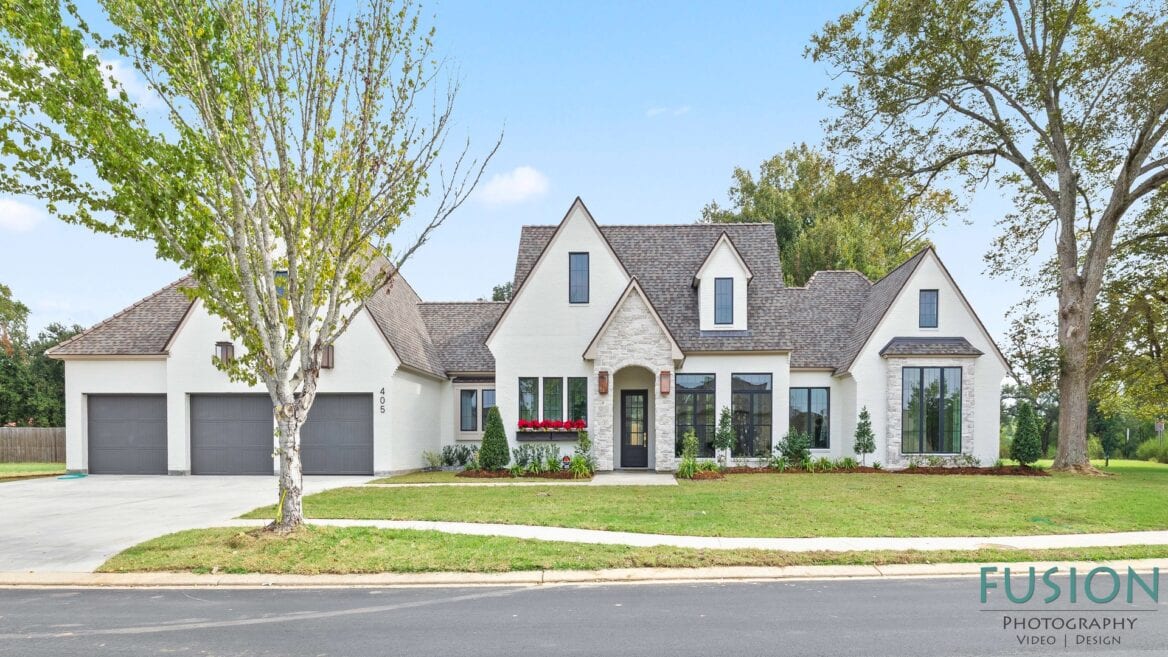 A white brick house with a multi-gabled roof, a three-car garage, and a front entry framed by light-colored stone.