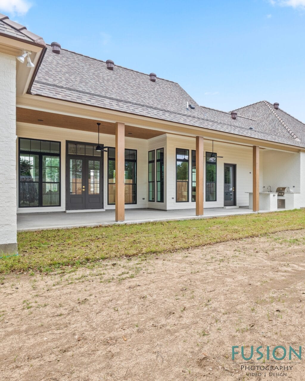 Back exterior of a white brick house with a covered patio, wooden support columns, and an outdoor grill station.