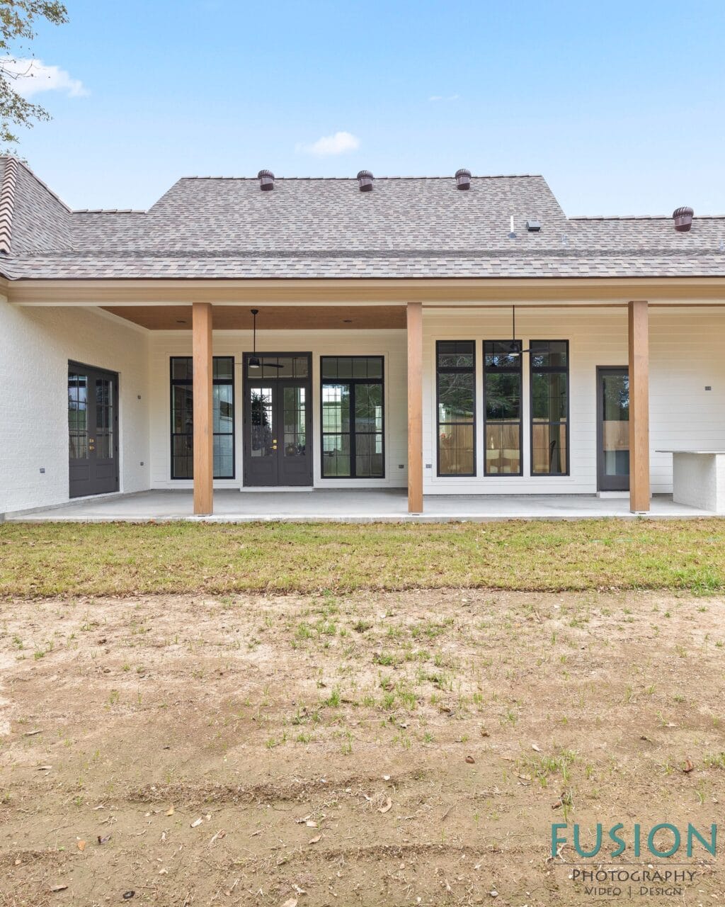 Back view of a white brick house with a covered patio, wooden support posts, and black-framed windows and doors.
