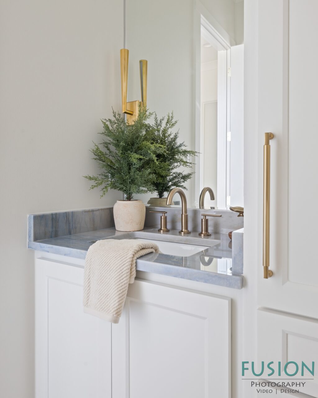 A bathroom vanity with a blue-veined marble countertop, brass fixtures, a potted green plant, and a beige towel draped over the sink.