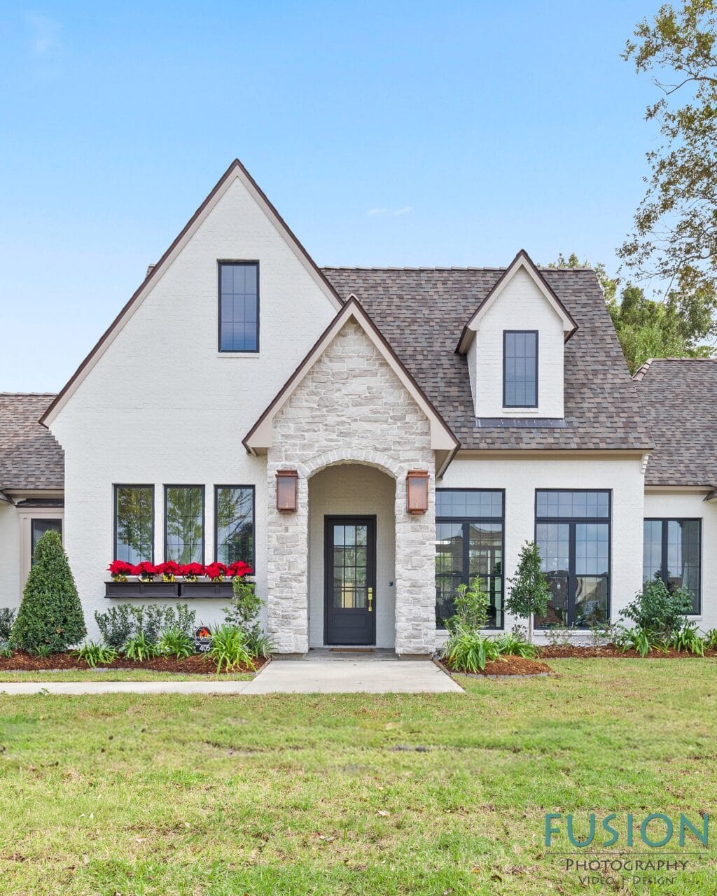 A white-painted brick house with a stone arched entryway, dark-framed windows, and red poinsettias in a window box.