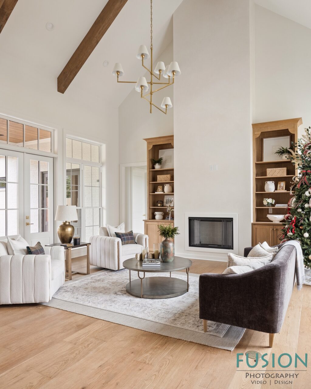 A living room with a vaulted ceiling, a fireplace flanked by wooden built-in shelves, a round coffee table, and an arrangement of upholstered armchairs and a sofa.