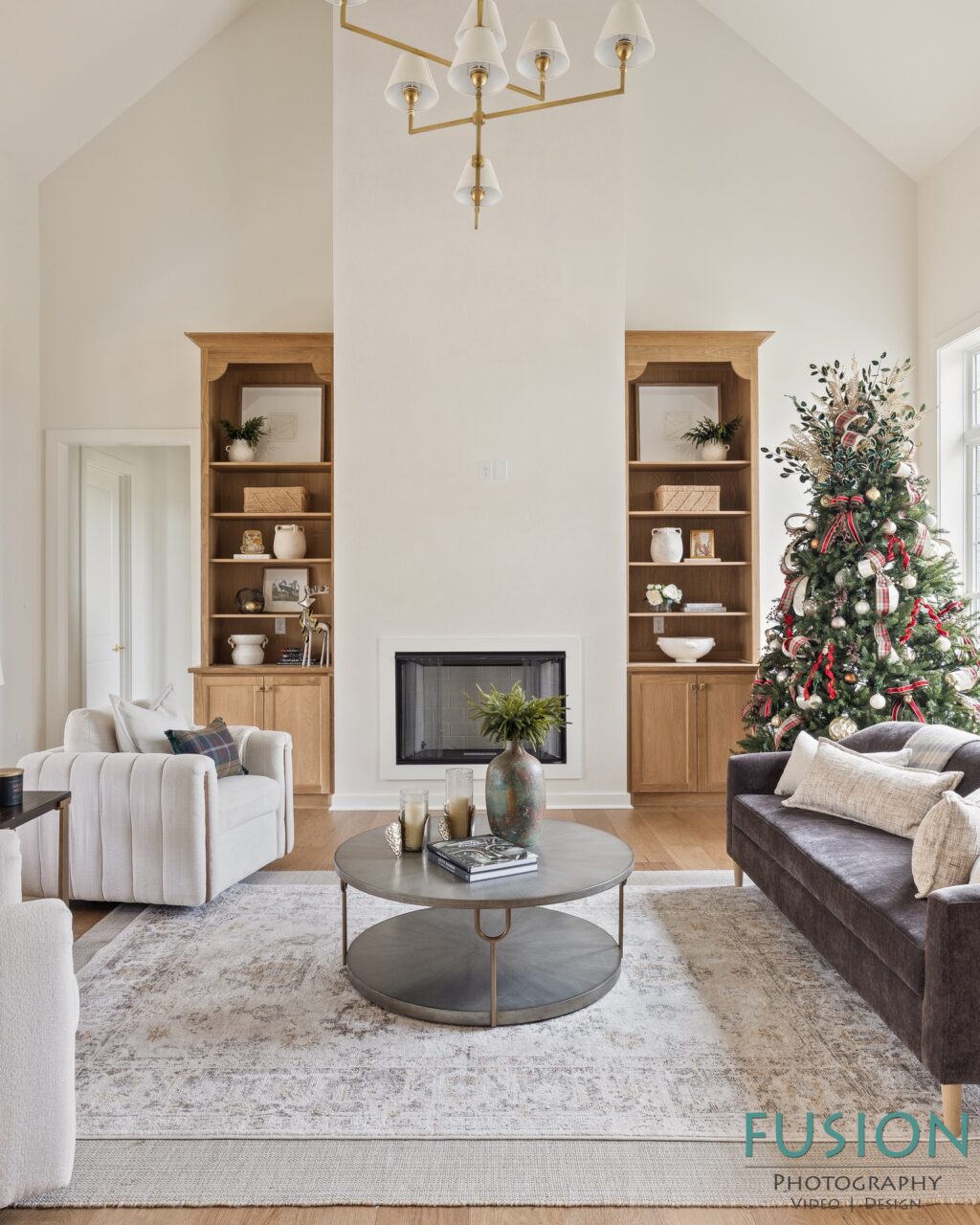 A living room with a fireplace centered between two built-in wooden bookshelves, a decorated Christmas tree, a circular coffee table, and upholstered seating.