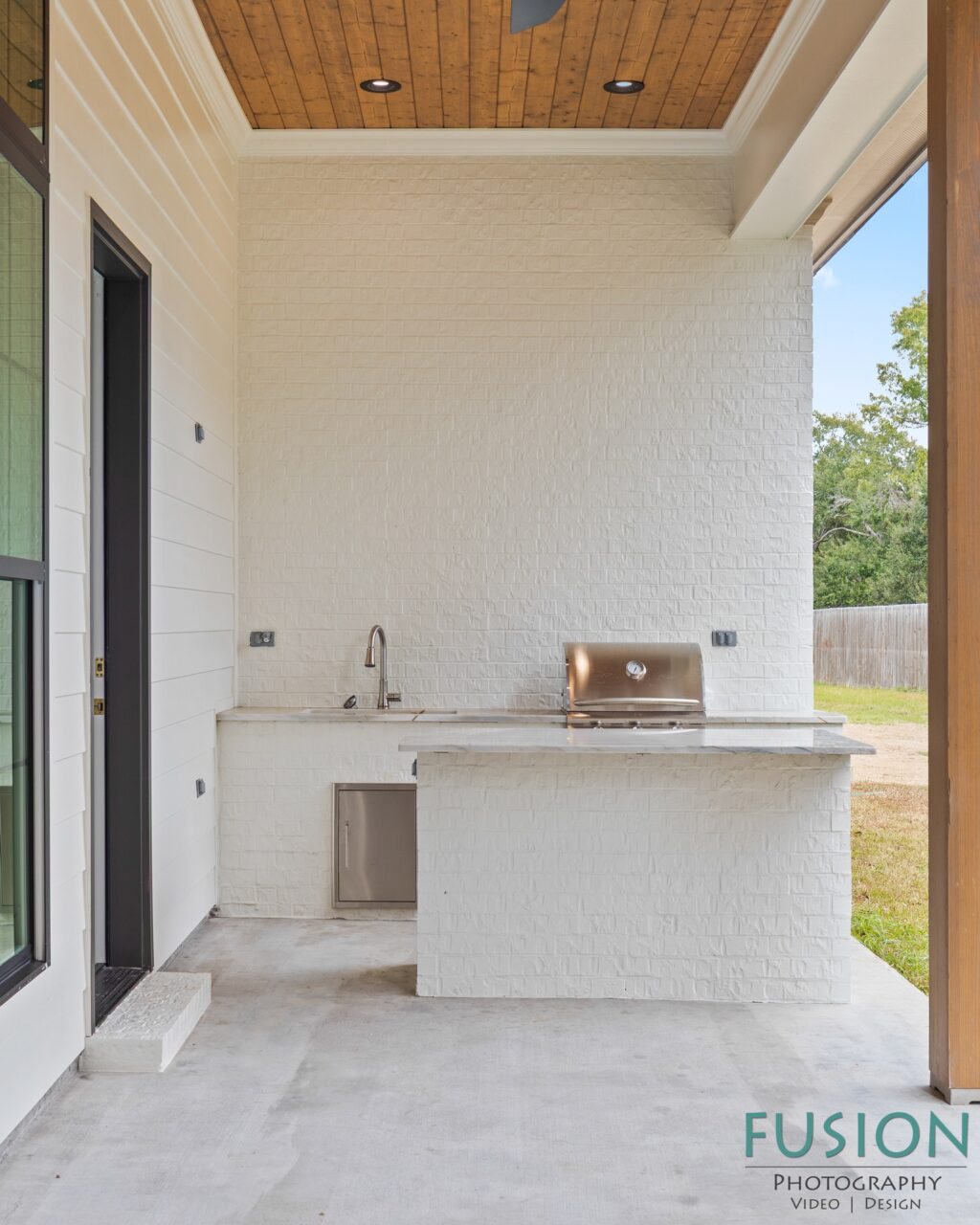 Outdoor kitchen on a covered patio with a white brick counter, built-in grill, sink, and storage cabinet.