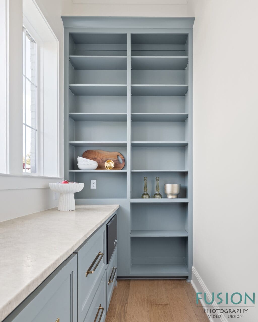 A built-in, blue-grey shelving unit next to a window with a stone countertop and a partially visible appliance.