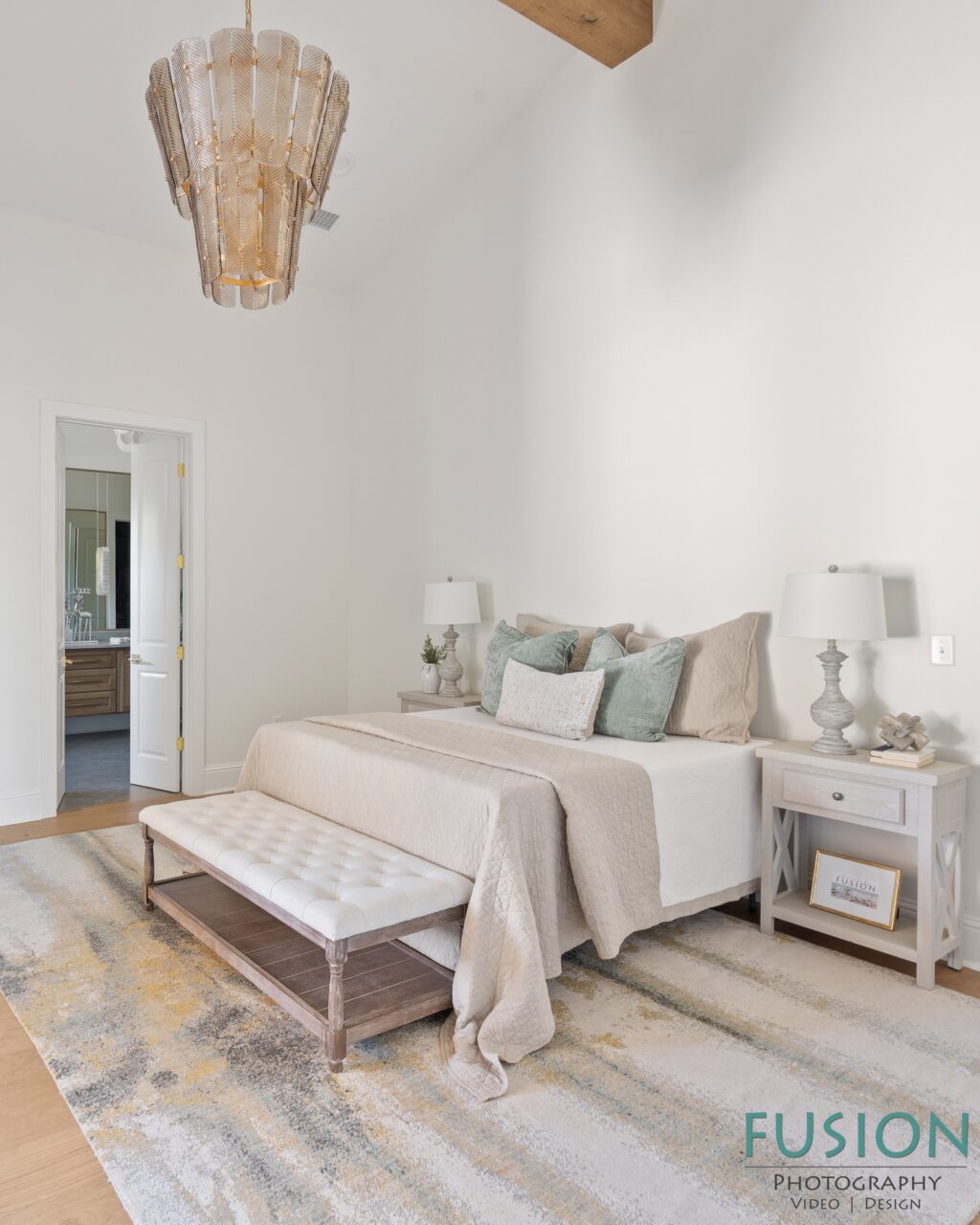 A bedroom featuring a bed with neutral bedding and light green accent pillows, flanked by two nightstands and topped with a tiered glass chandelier.