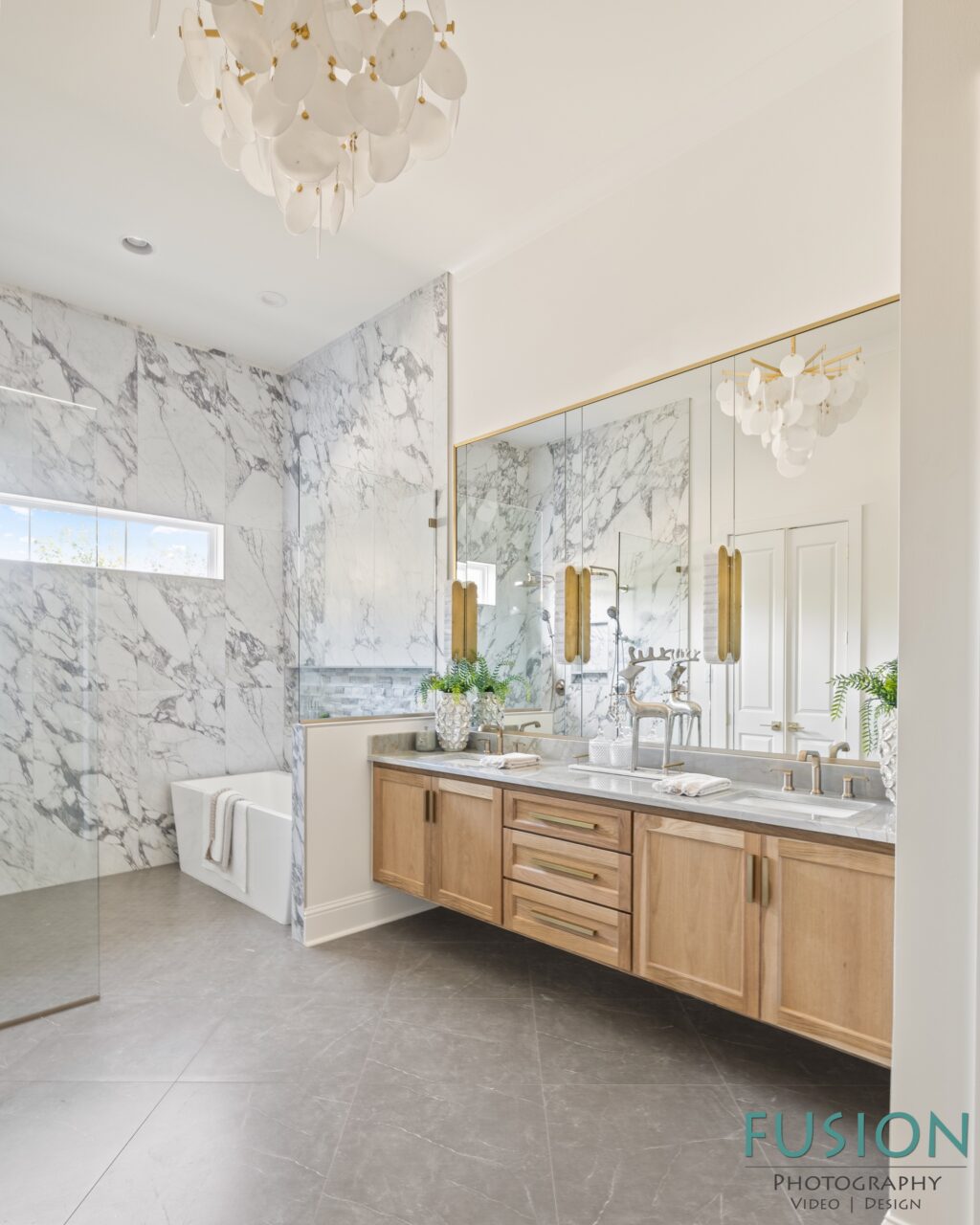 A modern bathroom with marble walls, a soaking tub, and a wooden double vanity beneath a large mirror.