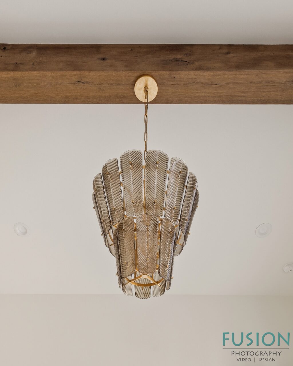 A tiered chandelier featuring metallic, leaf-shaped panels suspended from a wooden ceiling beam.