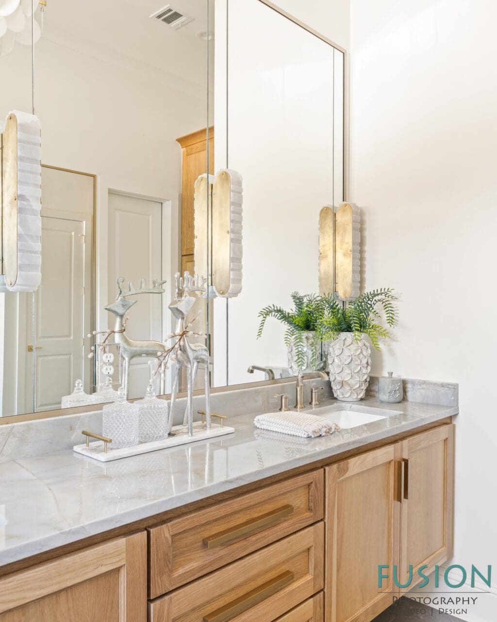 Bathroom vanity with a marble countertop, light wood cabinets, and two silver reindeer figurines on a tray.