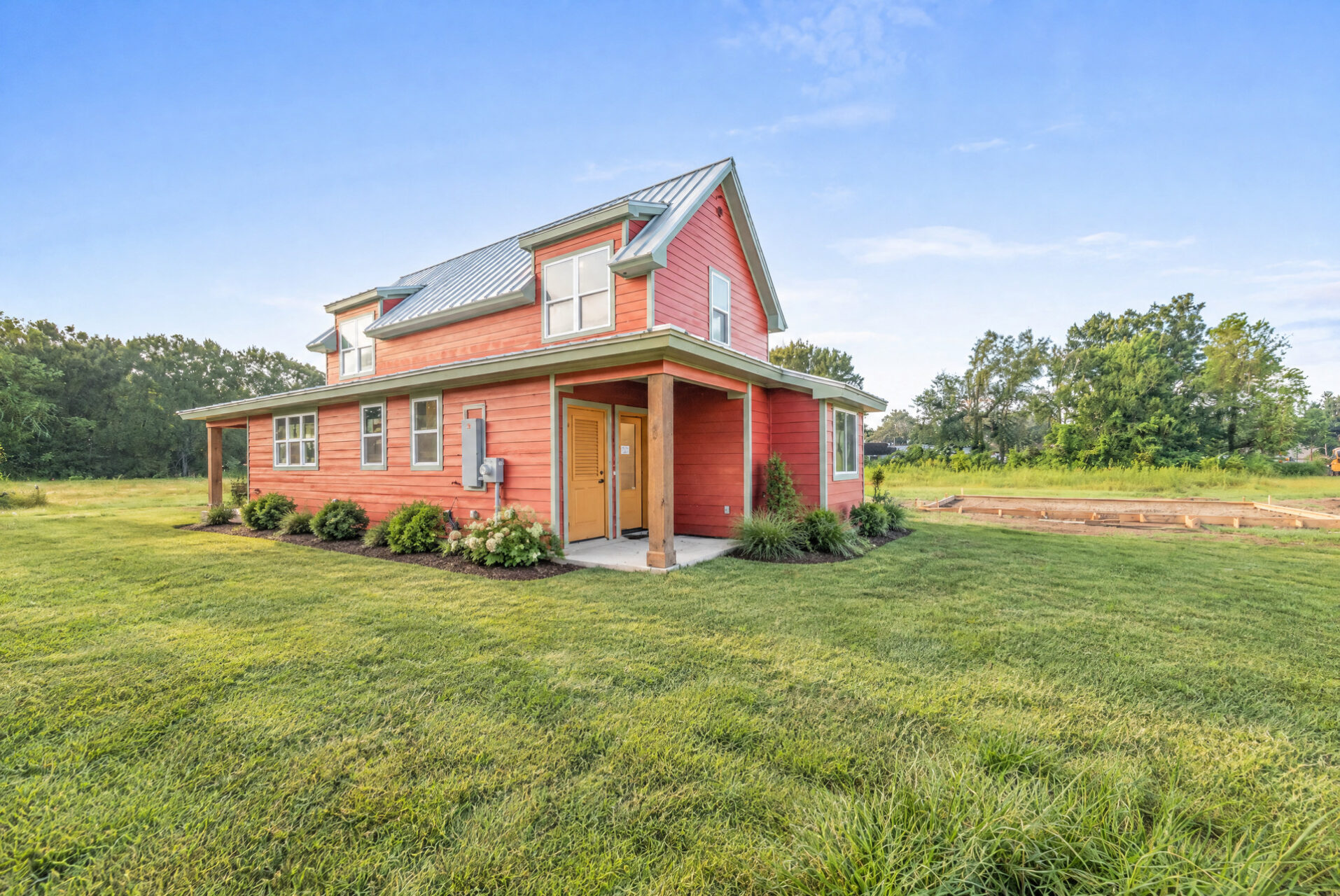 A red house with a metal roof and yellow doors sits on a grassy lawn.
